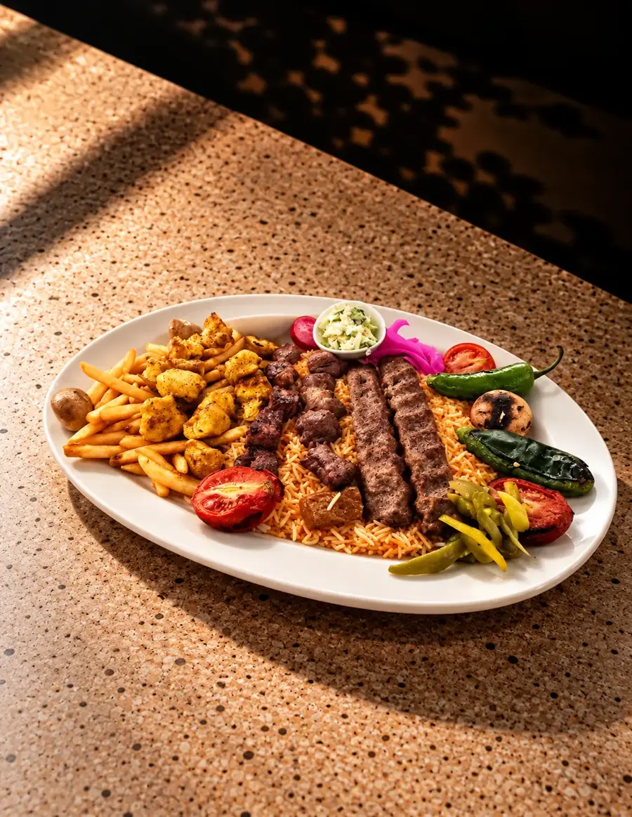 A platter of charcoal-grilled kabab and shish tawook with fries, grilled peppers, pickles and garlic sauce, lit by a low sun across a stone table.